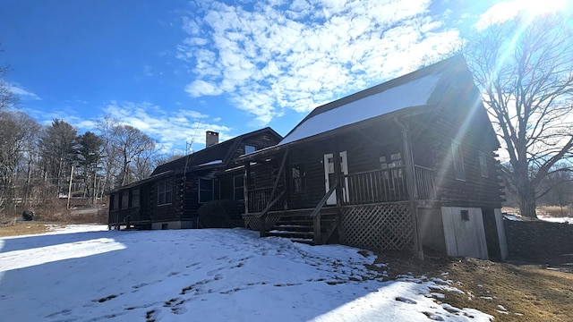 snow covered property featuring a chimney and log siding