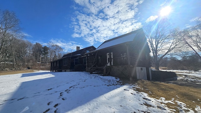 view of snowy exterior featuring a chimney and log siding