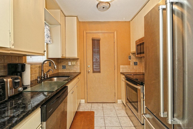 kitchen featuring light tile patterned floors, stainless steel appliances, backsplash, a sink, and dark stone countertops