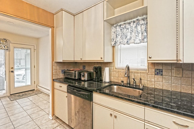 kitchen with light tile patterned floors, decorative backsplash, stainless steel dishwasher, a sink, and dark stone counters