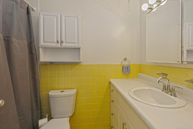 full bath with toilet, a wainscoted wall, a shower with curtain, vanity, and tile walls