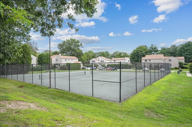 view of tennis court with a yard, a residential view, and fence