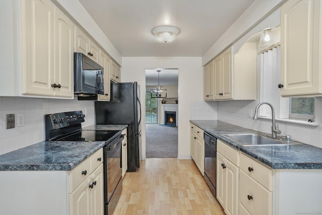 kitchen featuring a lit fireplace, black appliances, dark countertops, and a sink