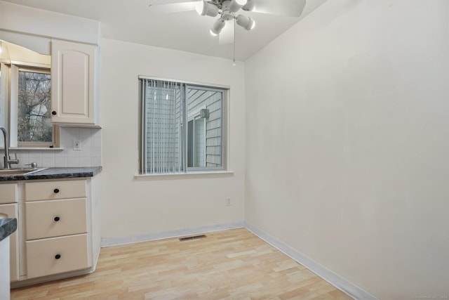 unfurnished dining area featuring light wood-type flooring, ceiling fan, baseboards, and a sink