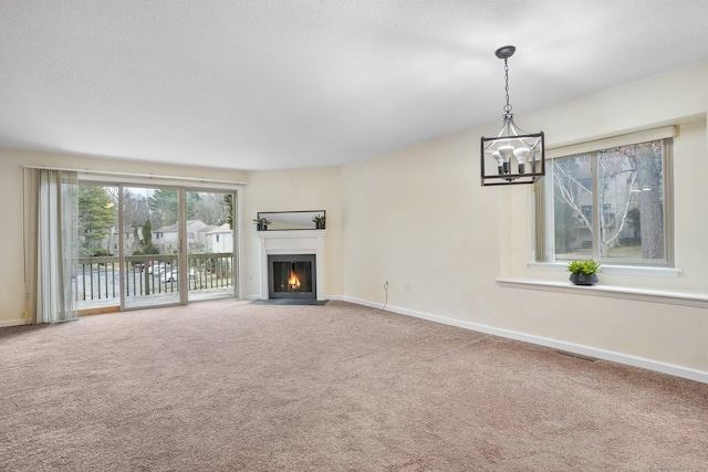 unfurnished living room with visible vents, baseboards, a fireplace with flush hearth, carpet flooring, and a notable chandelier