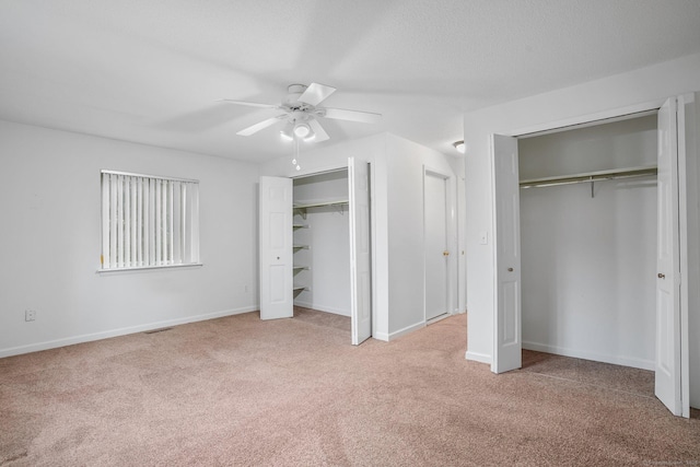 unfurnished bedroom with ceiling fan, visible vents, baseboards, carpet, and two closets