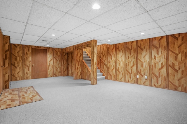 finished basement featuring carpet, recessed lighting, wood walls, a drop ceiling, and stairs