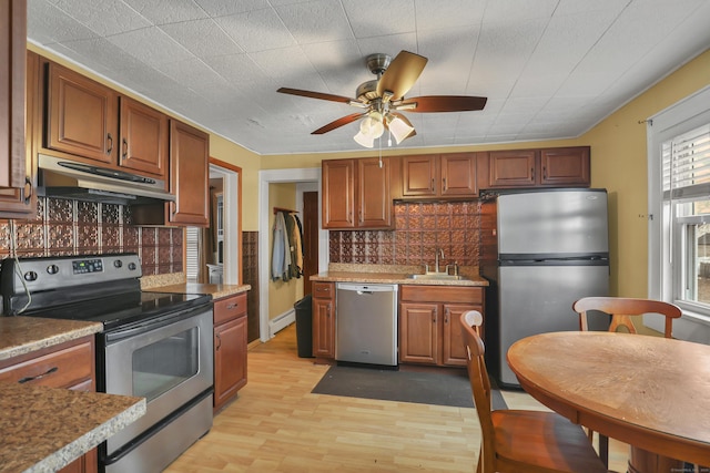 kitchen featuring under cabinet range hood, a sink, appliances with stainless steel finishes, backsplash, and light wood finished floors