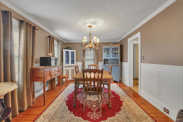 dining area with a textured ceiling, a notable chandelier, baseboard heating, light wood-type flooring, and wainscoting