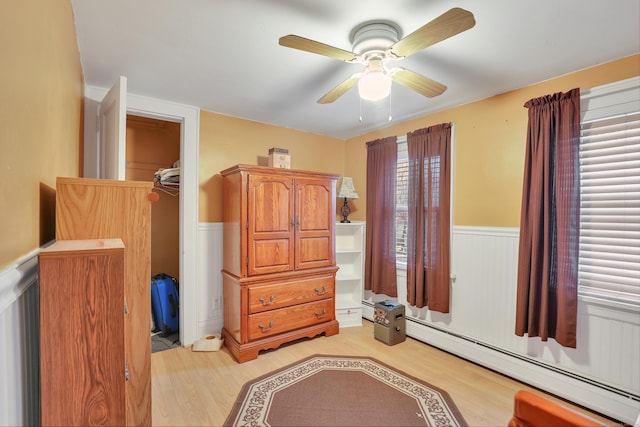 bedroom with a baseboard heating unit, light wood-type flooring, wainscoting, and ceiling fan