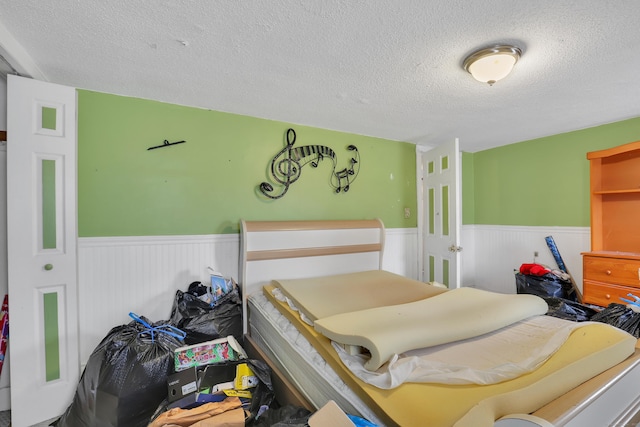 bedroom featuring a textured ceiling and wainscoting