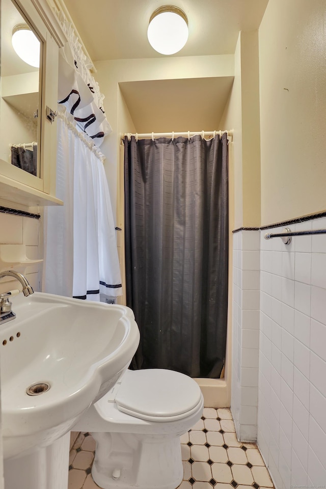 full bathroom featuring a wainscoted wall, tile walls, toilet, a stall shower, and a sink