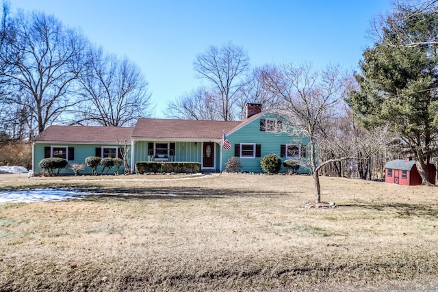 view of front of home featuring a chimney, an outdoor structure, a shed, a porch, and a front yard