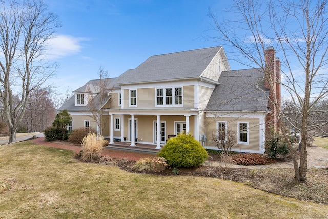 view of front of property featuring covered porch, a chimney, and a front lawn