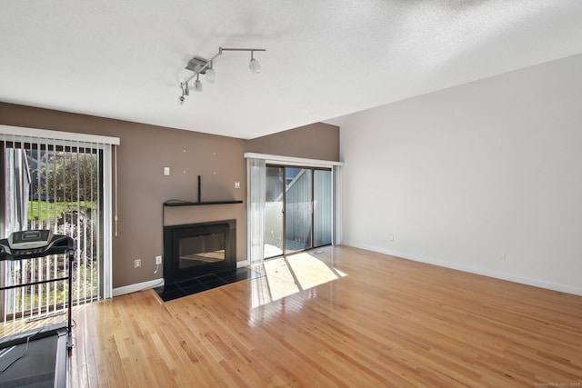 unfurnished living room featuring a fireplace with flush hearth, a textured ceiling, wood finished floors, and baseboards