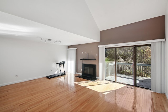 unfurnished living room featuring high vaulted ceiling, a fireplace with flush hearth, wood finished floors, baseboards, and rail lighting