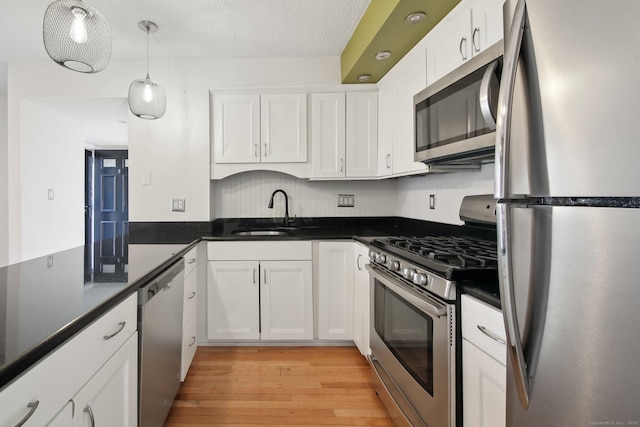 kitchen featuring a sink, white cabinetry, appliances with stainless steel finishes, light wood finished floors, and dark countertops