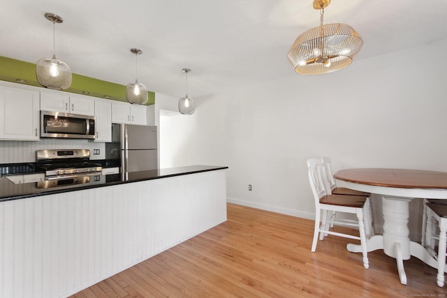 kitchen featuring stainless steel appliances, white cabinets, light wood-type flooring, dark countertops, and pendant lighting