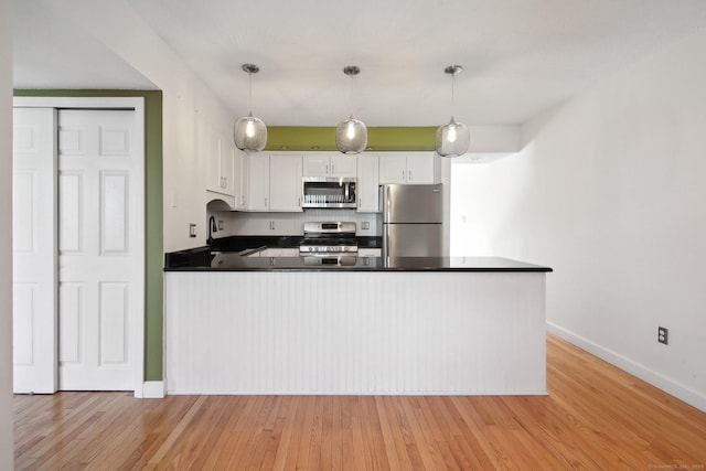 kitchen with stainless steel appliances, dark countertops, white cabinets, light wood-type flooring, and a peninsula