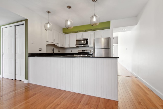 kitchen with stainless steel appliances, dark countertops, light wood-style flooring, white cabinetry, and a peninsula