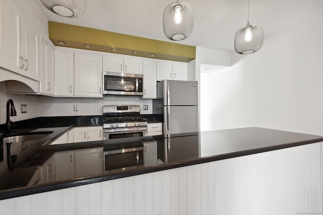 kitchen featuring white cabinets, dark countertops, appliances with stainless steel finishes, decorative light fixtures, and a sink