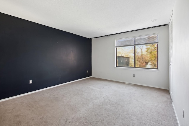 carpeted spare room with a textured ceiling and baseboards