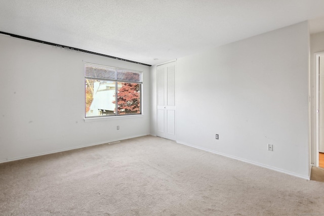 spare room with a textured ceiling, baseboards, and light colored carpet