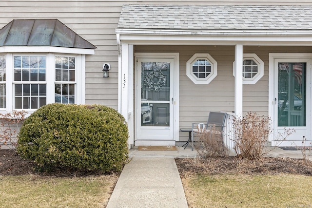 doorway to property featuring a porch and roof with shingles