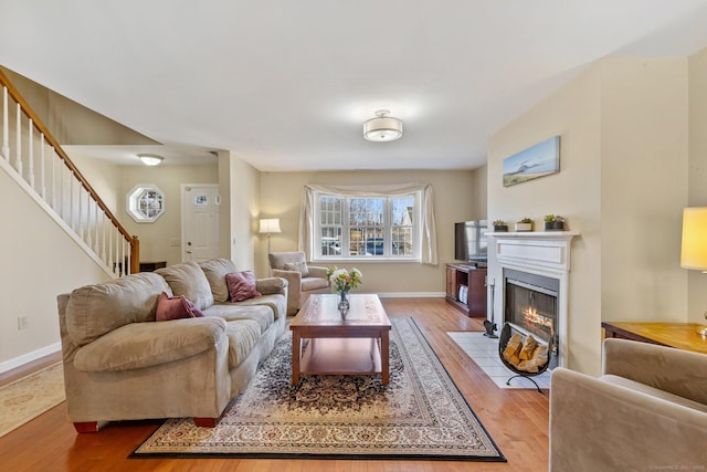 living area with stairway, a fireplace with flush hearth, baseboards, and light wood-style floors