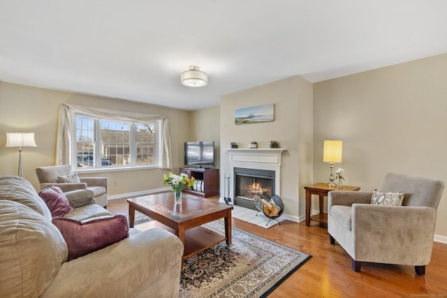 living area with baseboards, a fireplace with flush hearth, and wood finished floors