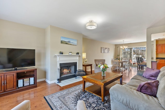 living area featuring a notable chandelier, a fireplace with flush hearth, baseboards, and light wood-type flooring