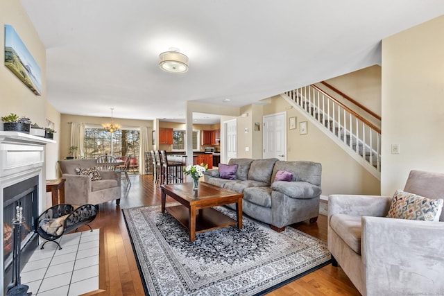 living room featuring a notable chandelier, stairway, a fireplace with flush hearth, and light wood-style flooring