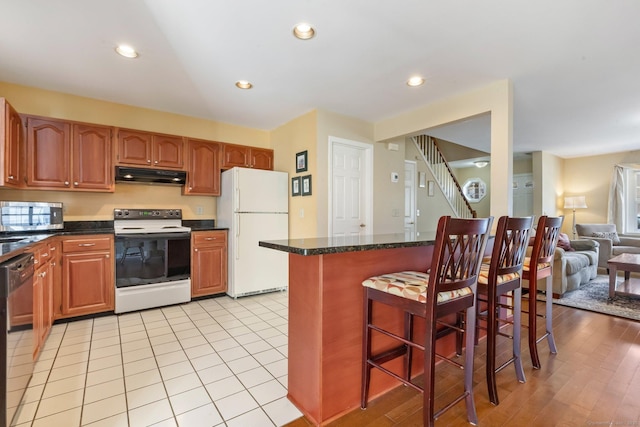 kitchen featuring under cabinet range hood, recessed lighting, white appliances, and a breakfast bar area