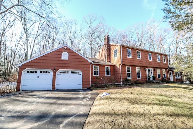 colonial inspired home with a garage, fence, driveway, a front lawn, and a chimney