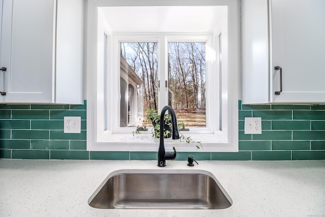 kitchen featuring white cabinets, a sink, decorative backsplash, and light stone countertops