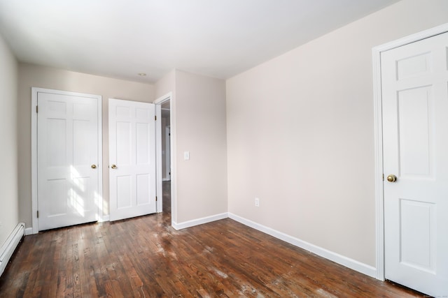 unfurnished bedroom featuring a closet, baseboard heating, dark wood finished floors, and baseboards