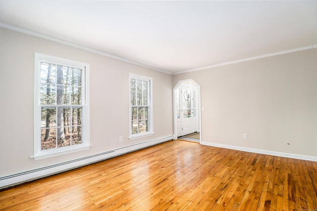 empty room featuring a wealth of natural light, a baseboard radiator, ornamental molding, and light wood finished floors