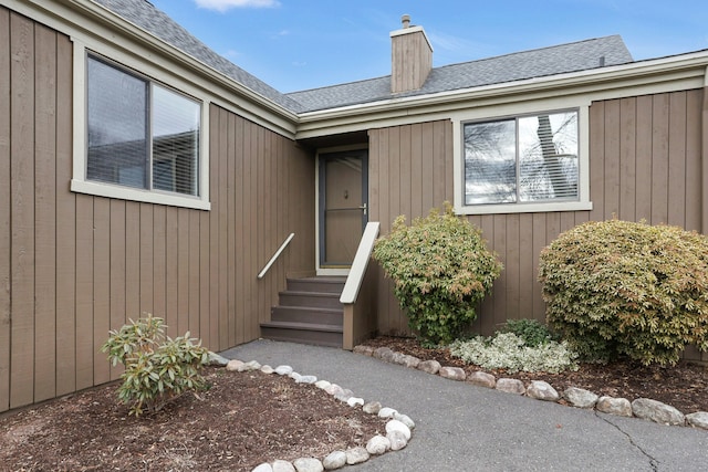 doorway to property with a chimney and a shingled roof