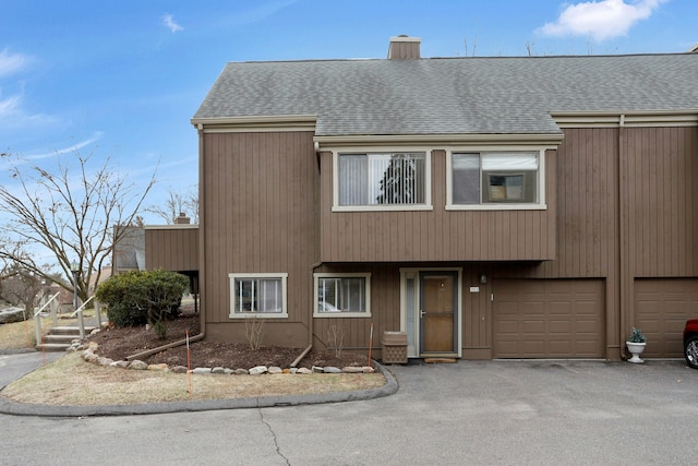 multi unit property featuring roof with shingles, a garage, driveway, and a chimney