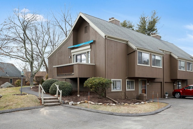 view of front of home with an attached garage, a chimney, driveway, and a shingled roof