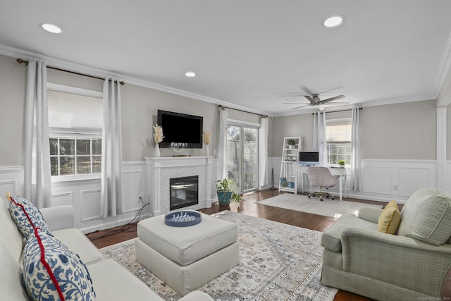 living area with wainscoting, crown molding, wood finished floors, and a glass covered fireplace