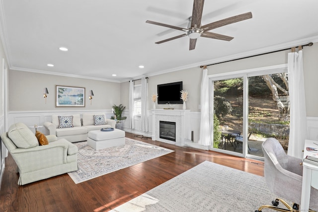 living room featuring recessed lighting, wood finished floors, ornamental molding, wainscoting, and a glass covered fireplace