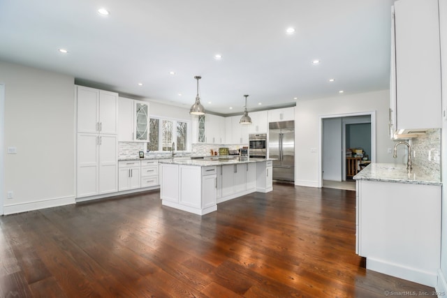 kitchen with dark wood-style flooring, a kitchen island, white cabinetry, appliances with stainless steel finishes, and glass insert cabinets