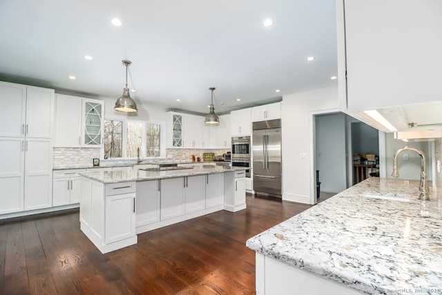 kitchen featuring a kitchen island, glass insert cabinets, appliances with stainless steel finishes, a sink, and backsplash