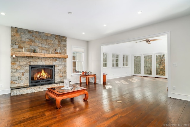 living area featuring baseboards, a stone fireplace, hardwood / wood-style floors, and a healthy amount of sunlight