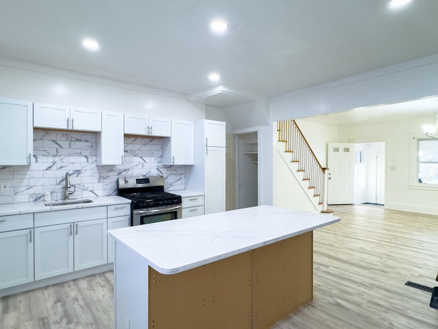 kitchen with stainless steel range with gas cooktop, light wood-style flooring, decorative backsplash, a sink, and light stone countertops