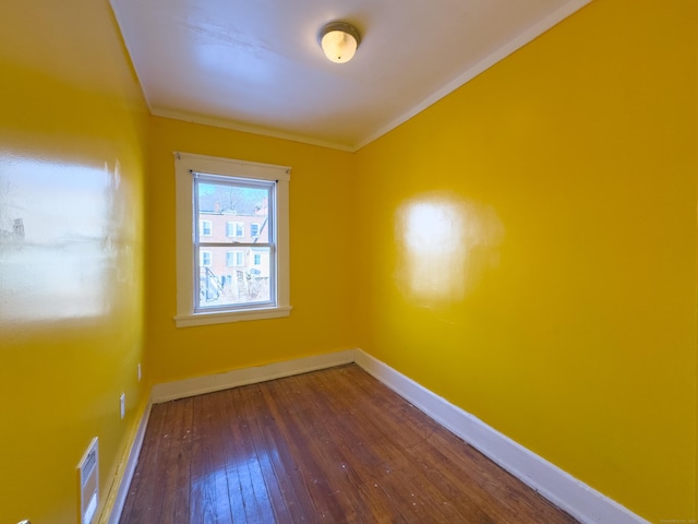 empty room featuring ornamental molding, wood-type flooring, visible vents, and baseboards