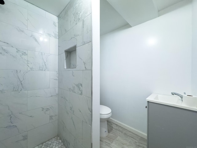 full bath featuring toilet, baseboards, tiled shower, and vanity