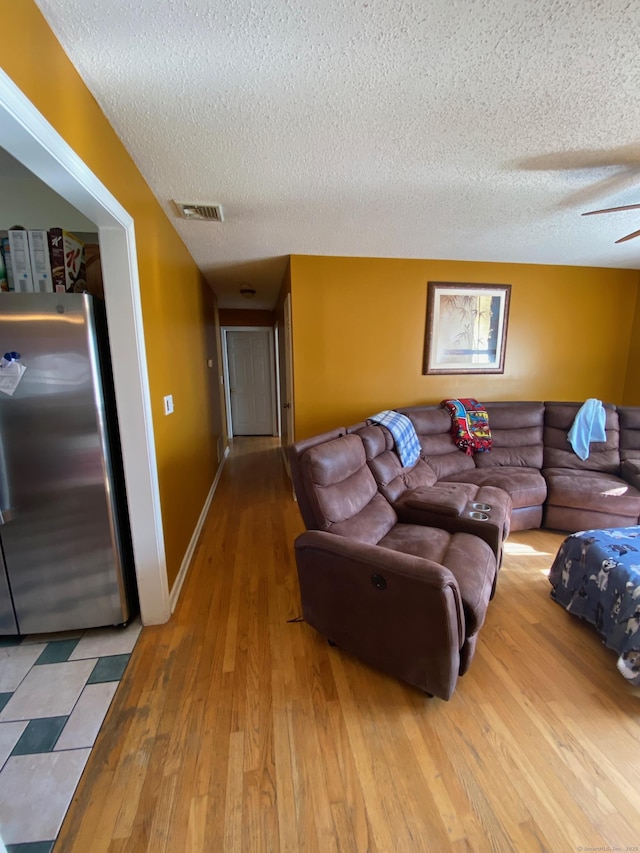 living room featuring a textured ceiling, ceiling fan, wood finished floors, visible vents, and baseboards