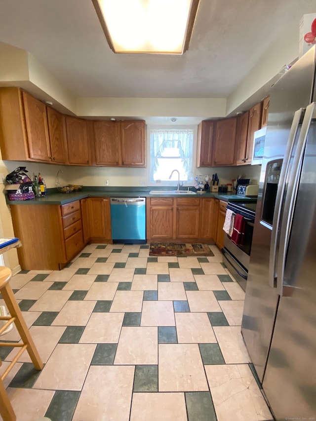 kitchen with dark countertops, appliances with stainless steel finishes, brown cabinets, and a sink